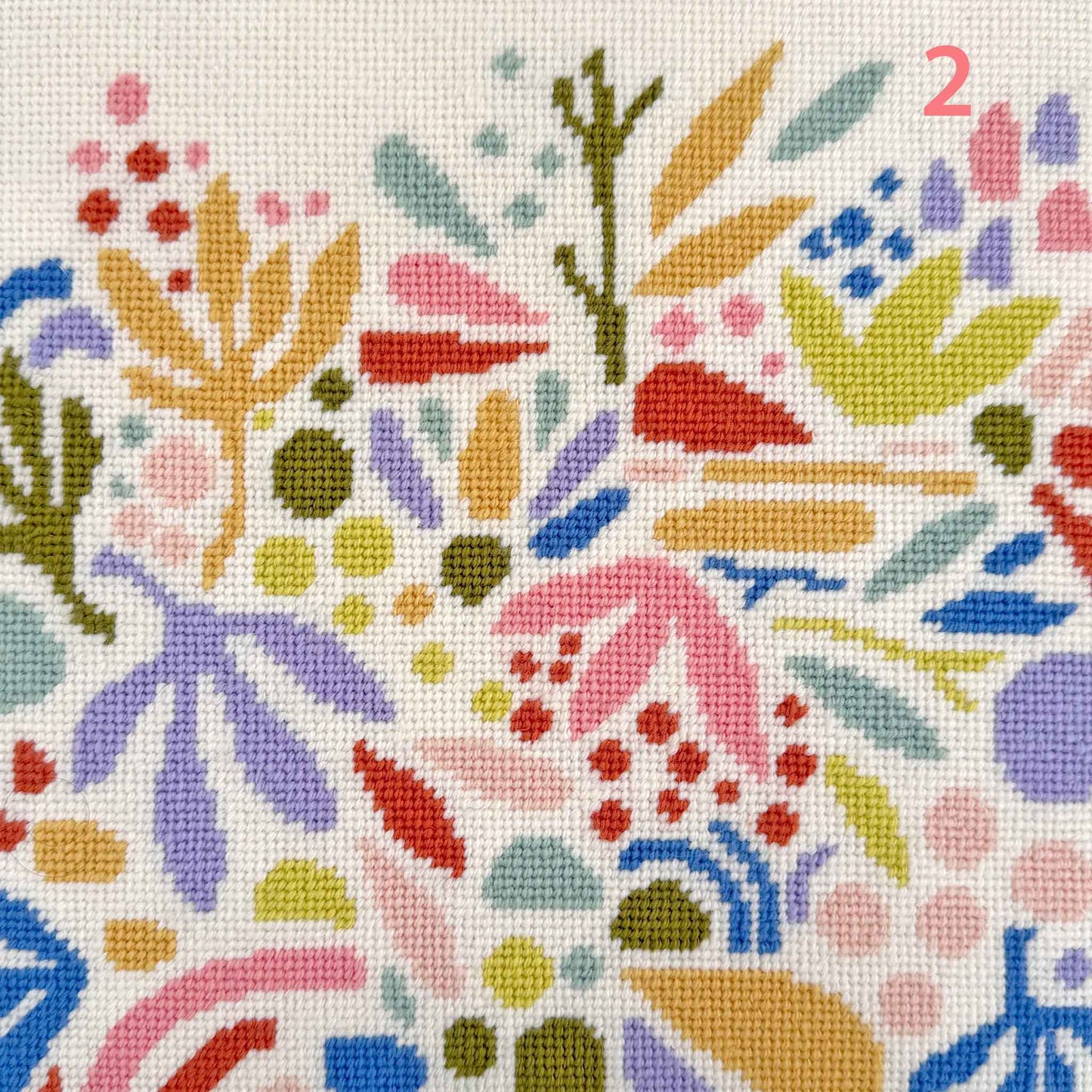modern needlepoint of floating abstract leaves and shapes in corals, lilac and gold colours on a cream ground