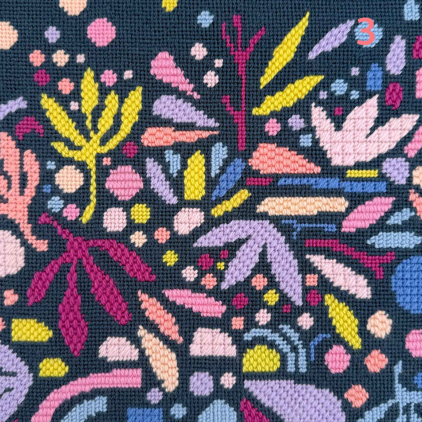 modern needlepoint of floating abstract leaves and shapes in pinks, purples and blues on a dark teal ground