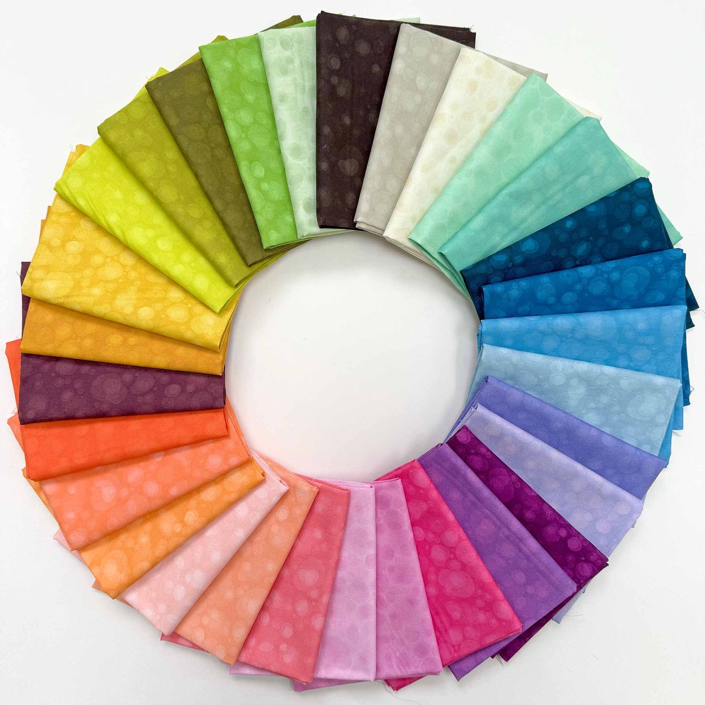 A ring of 30 colours of folded fabrics with a mottled, tonal print arranged on a white ground