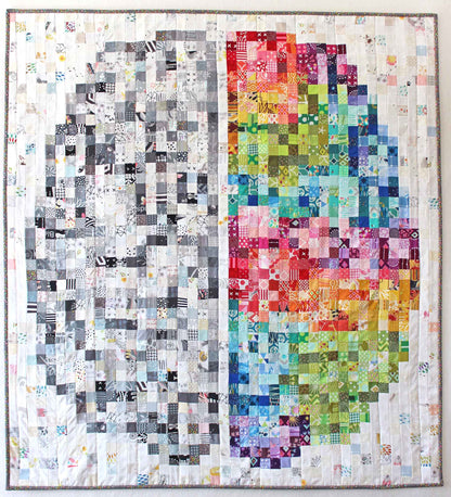 quilt showing a pixelated brain, half black, grey and white, half rainbow coloured on a low-volume ground with dark grey binding