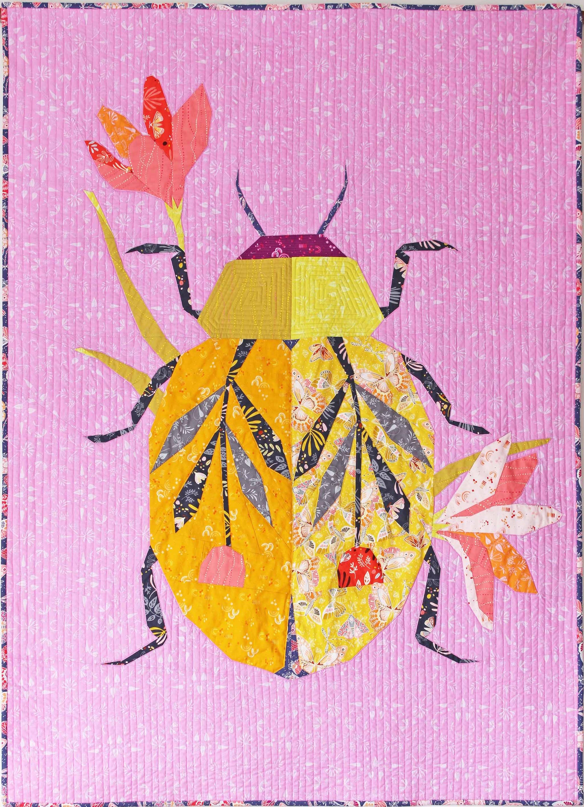 quilt of a large yellow beetle on a pink-purple ground with 2 flowers and leaves on wings