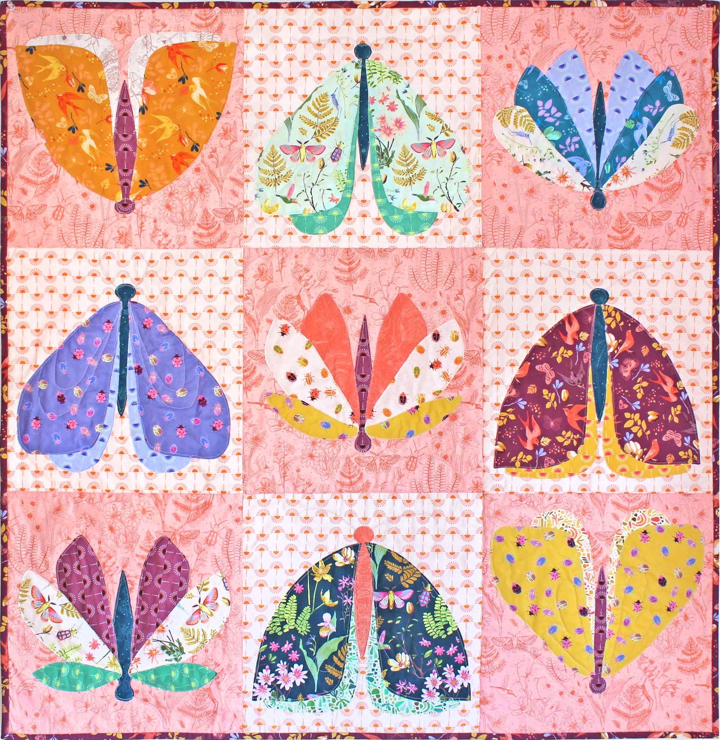 square quilt of 9 blocks, each with a large appliqué butterfly in multi colours on soft coral ground